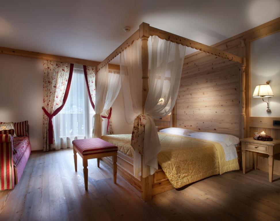 Mājas interjers ar gultu ar baldahīnu, koka mēbelēm un ziedu motīviem logu aizkaros. Gaismas avots un siltas krāsas rada mājīgu atmosfēru.