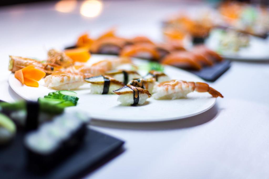 Svaiga sushi un garneles uz baltas šķīvja ar dārzeņu dekorācijām, radot pievilcīgu ēdiena kompozīciju.