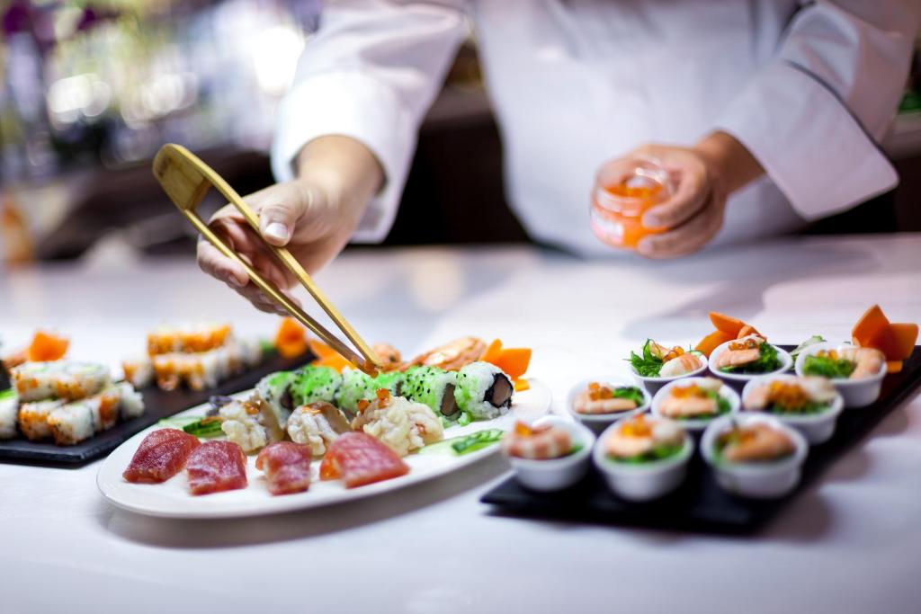 Sushi šefpavārs, izmantojot čīles, rūpīgi pasniedz dažādus sushi ēdienus un jūras veltes, radot elegantu un garšīgu prezentāciju.