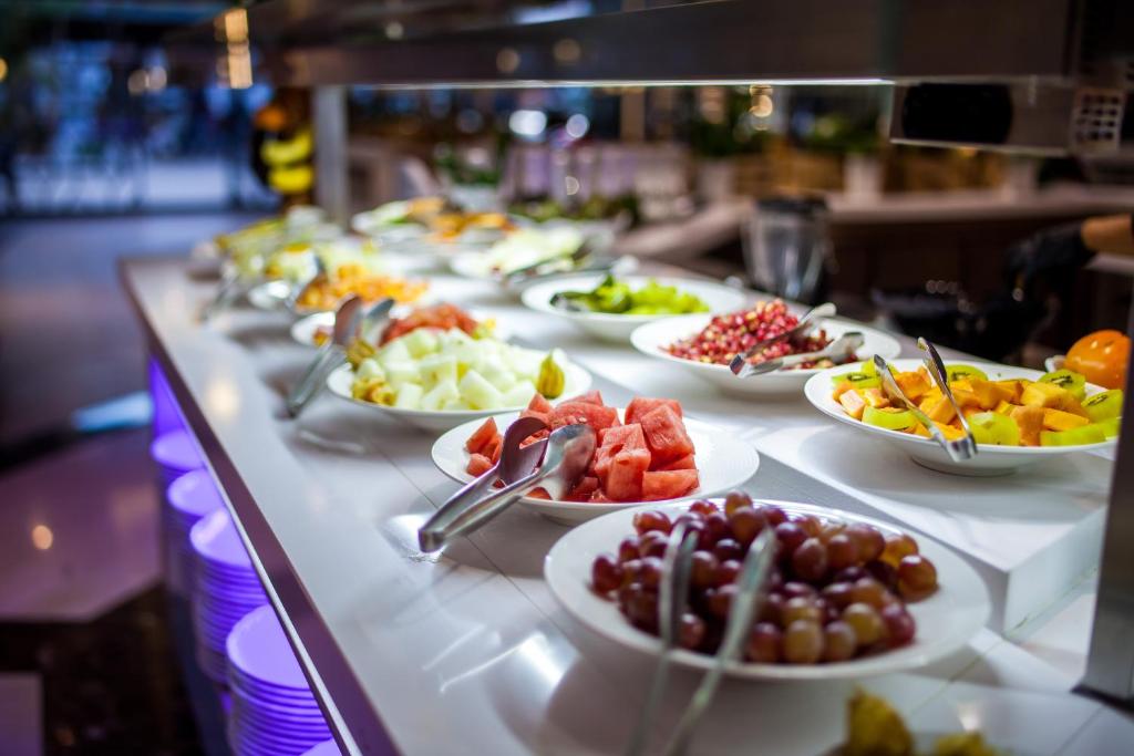 Bagātīgs augļu bufete ar dažādām salātiem, tostarp arbūziem, vīnogām un citām sezonas ogām. Ideāli piemērota veselīgai uzkodu izvēlei.