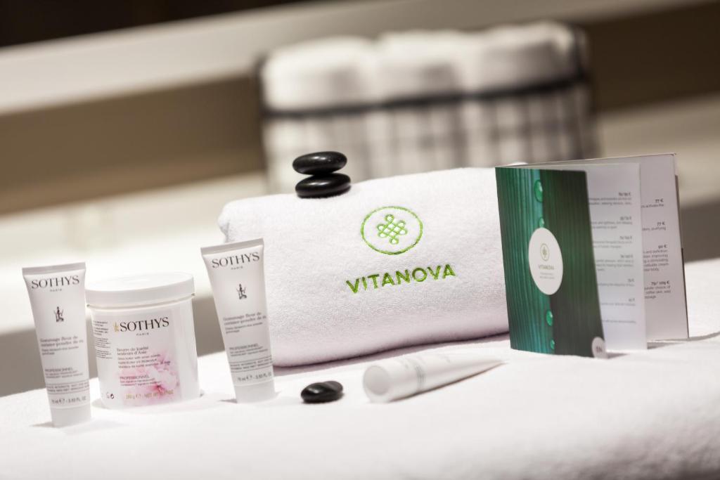 Kosmētikas un spa produktu komplekts uz baltas dvielīša, ietver Sothys produktus un Vitanova logotipu. Redzams arī pakalpojumu katalogs un akmens.