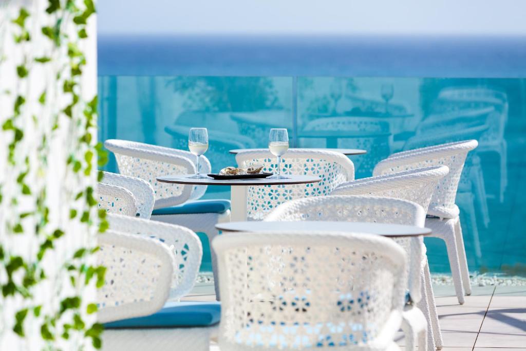 Eleganta terase ar baltām krēslām, galdiem un dzērieniem, kas piedāvā brīnišķīgu skatu uz jūru. Ideāla vieta relaksācijai un atpūtai.