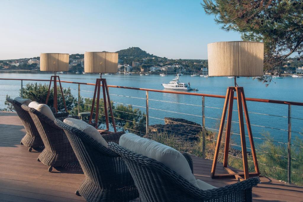 Terase ar skatu uz ūdeni, kur redzami eleganti krēsli un stilīgas lampas, kas rada relaksējošu atmosfēru. Fonā redzama jahta un ainavisks kalns.
