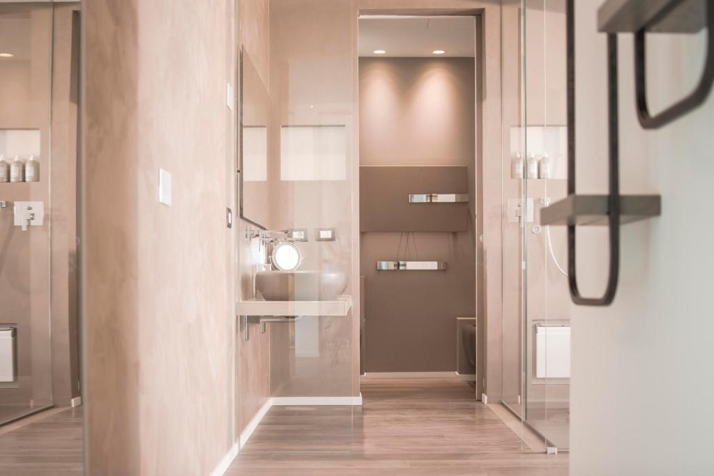 Mūsdienīgs vannas istabas interjers ar gaišām sienām, stikla dušu un minimālu dizainu. Telpa ir labi apgaismota un iekārtota ar elegantiem aksesuāriem.