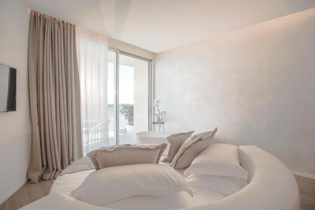 Mūsdienīga guļamistaba ar lieliem logiem, kur caur tiem ieplūst dabiska gaisma, un izsmalcinātu interjeru ar neitrālām krāsām un ērtu gultu.