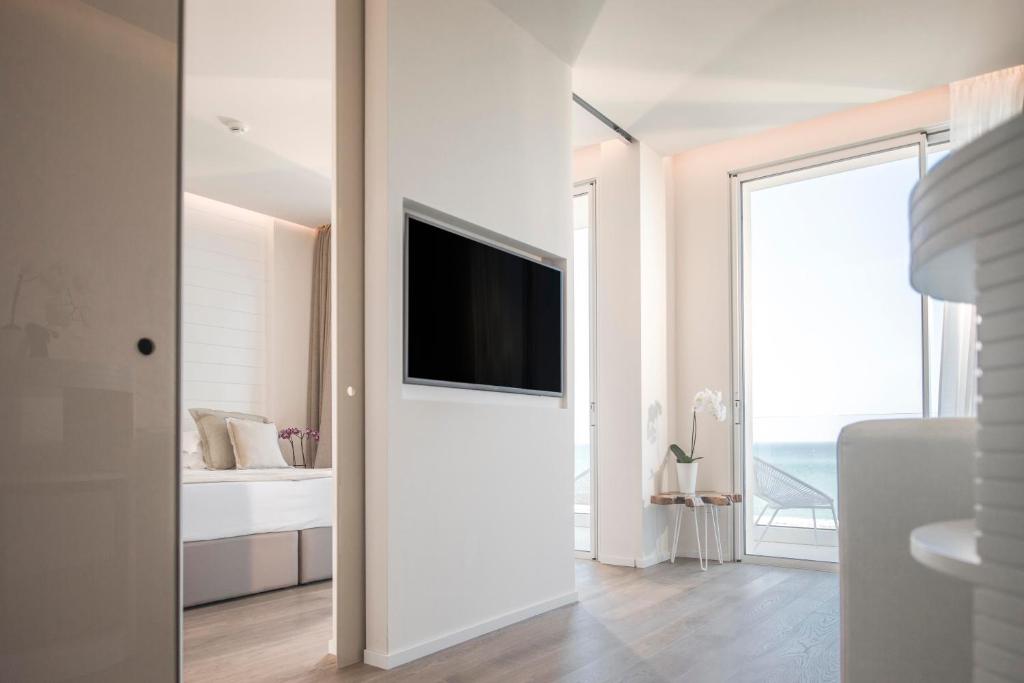 Mūsdienīgs interjers ar skatu uz jūru, kurā redzama guļamistaba un televizors uz sienas, radot relaksējošu atmosfēru.