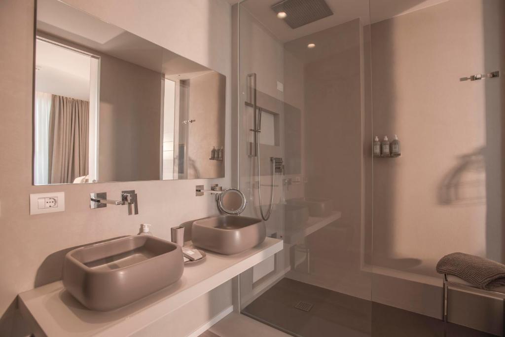 Mūsdienīgs vannas istabas interjers ar divām pelēkām izlietnēm, spoguļiem un dušas kabīni. Eleganti un minimālistiski dizaina elementi rada relaksējošu atmosfēru.