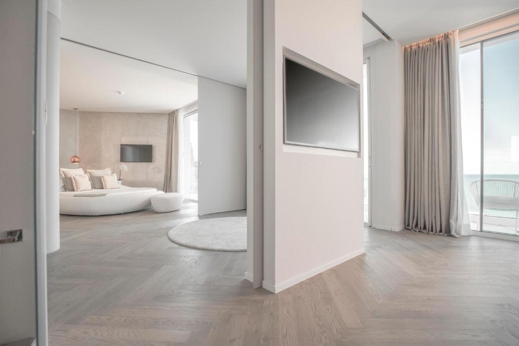 Mūsdienīga interjera dizaina telpa ar gaišām krāsām, modernu TV un komfortablu sēdvietu. Atvērta plānojuma pieeja rada plašuma sajūtu un gaismas ieplūšanu.