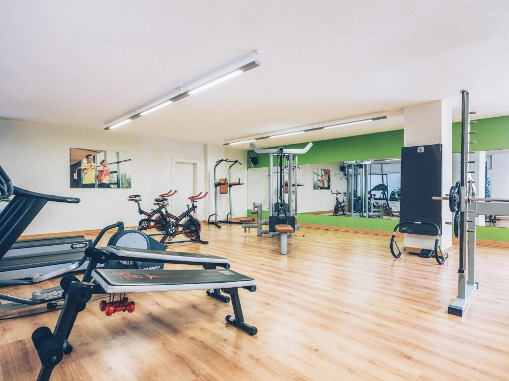 Mūsdienīgs sporta zāles interjers ar dažādiem trenažieriem un aprīkojumu, kas veicina aktīvu dzīvesveidu. Gaismas un zaļas sienas radījušas dinamisku un iedvesmojošu atmosfēru.