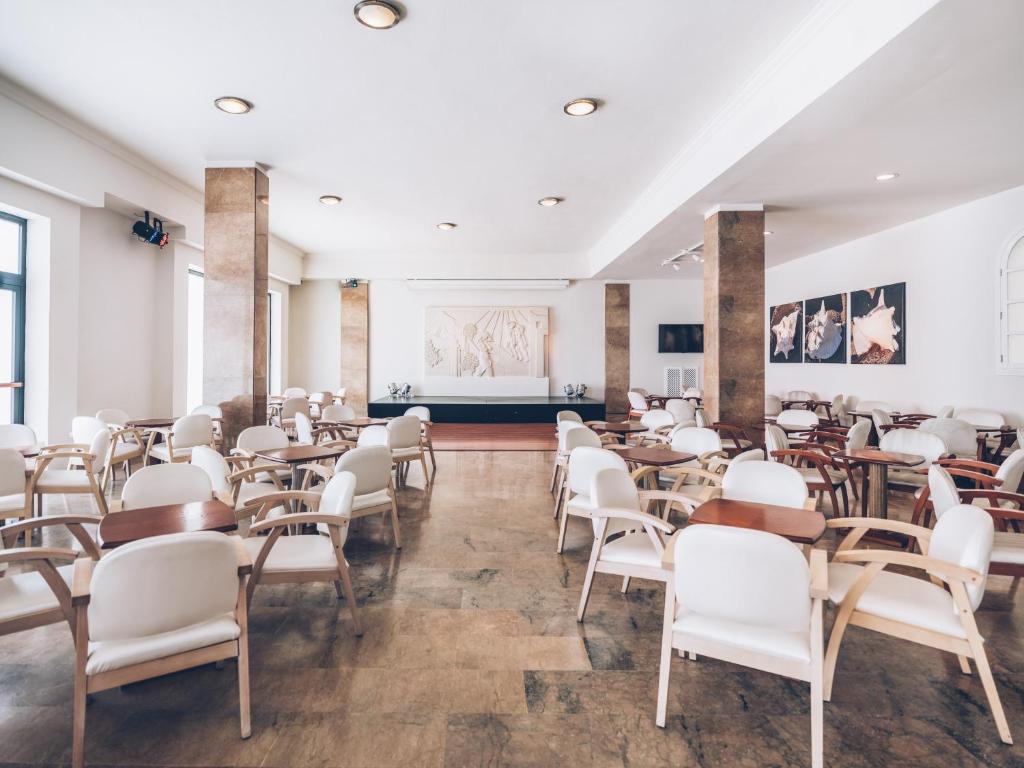 Moderns restorāns ar gaišām krāsām un elegantu interjeru, kurā ir baltas krēslus un koka galdiņus. Uz sienas redzama mākslinieciska kompozīcija un fotogrāfijas.