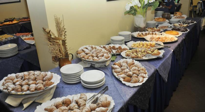 Saldumu bufete ar dažādiem konditorejas izstrādājumiem, tostarp cepumiem un tortēm, uz galda ar šķīvjiem un ziediem.