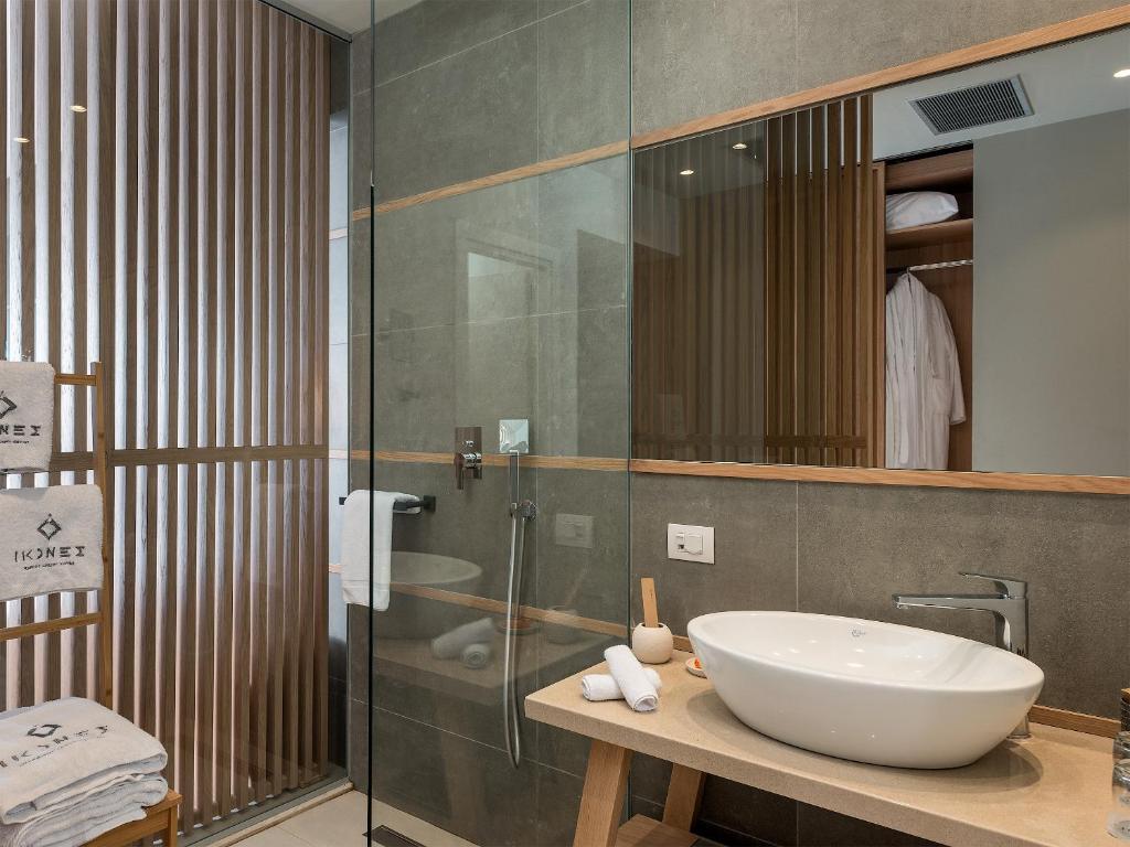 Mūsdienīgs vannas istabas interjers ar stikla dušu, akmens izlietni un koka akcentiem. Vannas dvieļi ir sakārtoti uz koka plaukta, radot elegantu un relaksējošu atmosfēru.