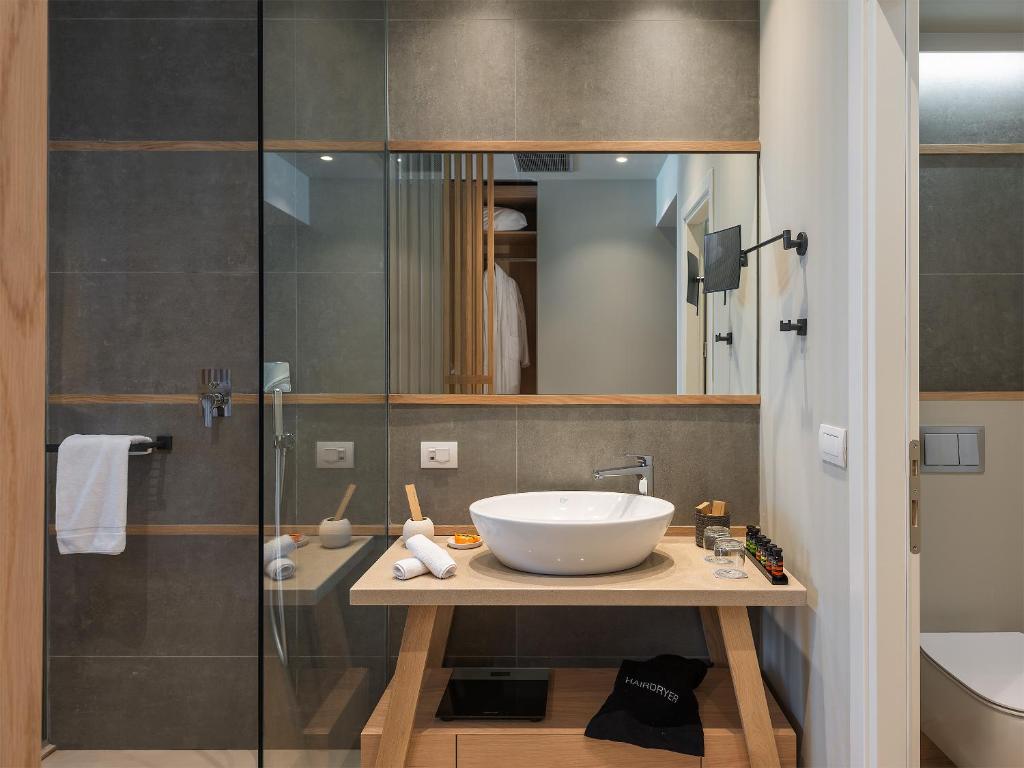 Mūsdienīga vannas istaba ar stikla dušu un elegantu izskatu, kur centrā ir stilīgs izlietnes galds ar apaļu izlietni un dažādi higiēnas piederumi.