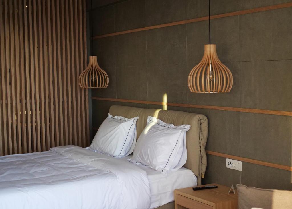 Mūsdienīga guļamistaba ar koka akcentiem, kurā ir divguļamā gulta ar baltām gultasveļām un stilīgām koka lampām. Sienas dekorētas ar vertikālām koka sliedēm, radot siltu un viesmīlīgu atmosfēru.