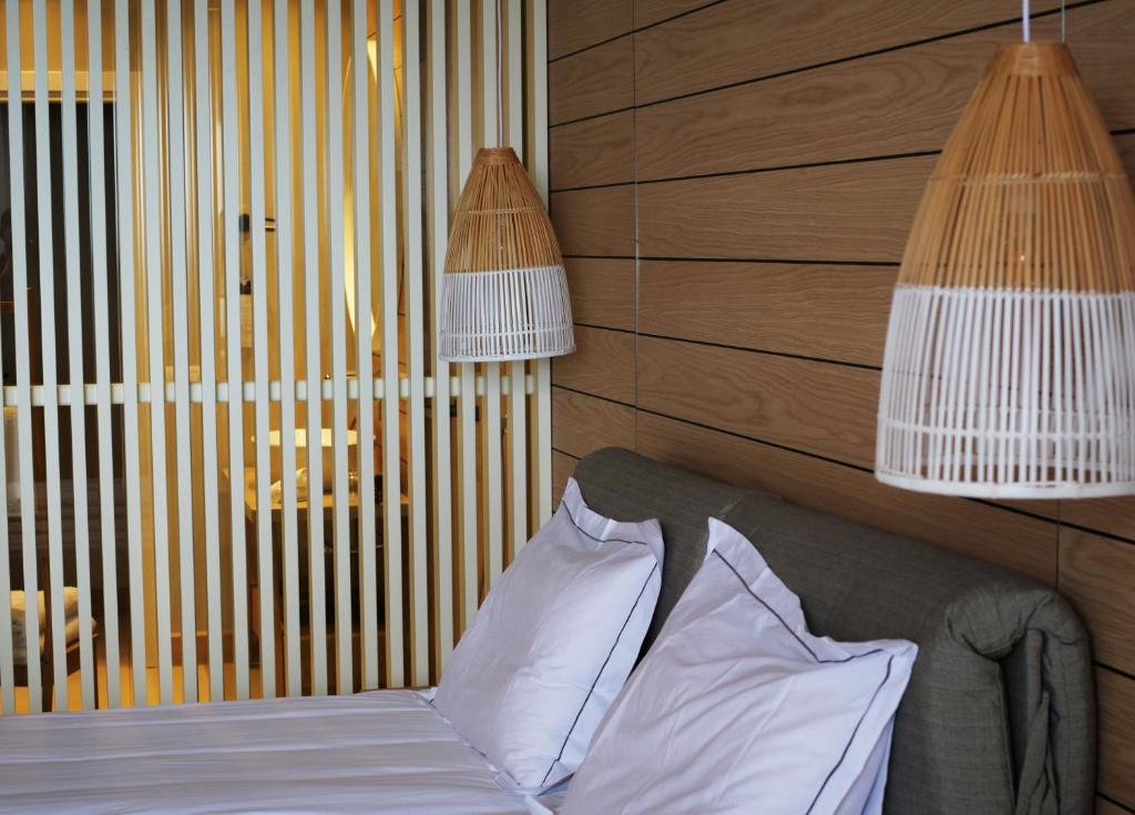 Moderns guļamistabas interjers ar koka apdari un dekoratīvām lampām. Gultā ir baltas spilveni, kas piešķir mājīgumu.