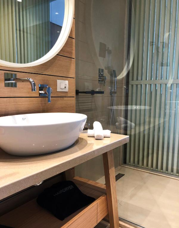 Moderns vannas istabas interjers ar apaļu spoguli, balto izlietni un dušu. Koka detaļas piešķir siltumu un eleganci.