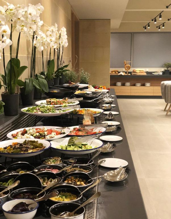 Bagātīgs bufetes galds ar dažādiem salātiem, uzkodām un ziedu dekorācijām, radot pievilcīgu un elegantu atmosfēru. Ideāls izvēle gardēžiem un svinībām.