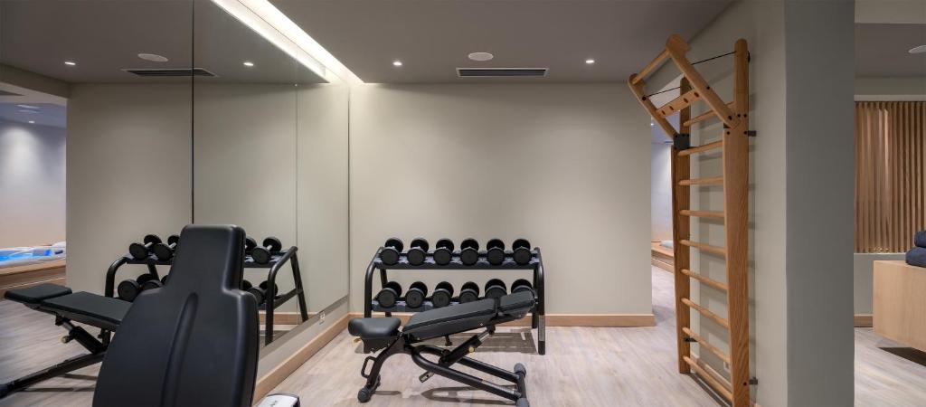 Mūsdienīgs trenažieru zāles interjers ar svaru stendiem, hantelēm un pievilkšanās stieni. Telpa ir gaiša un funkcionāla, nodrošinot ideālu vidi treniņiem.