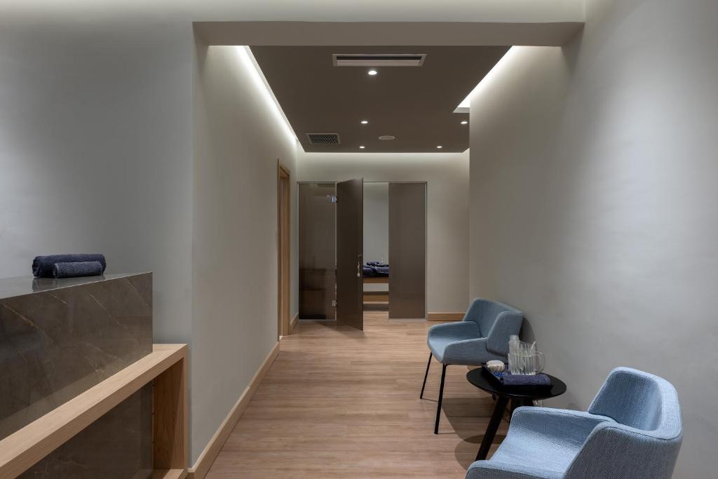 Mūsdienīgs spa gaiteņs ar koka grīdu un neitrālām krāsām, kurā redzami komfortabli krēsli un galdiņš ar ūdens karafēm. Paredzēts relaksācijai un atpūtai.