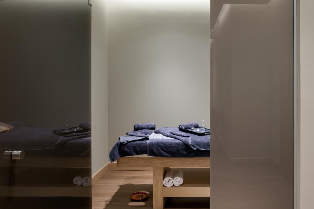 Relaksējoša masāžas telpa ar koka galdu, pārklātu ar tumši zilu dvieli, un dvieļiem uzglabāšanai. Telpa ir gaiša un mierīga, radot patīkamu atmosfēru.