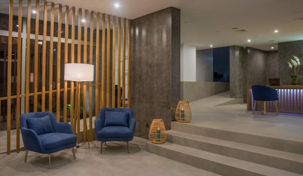 Mūsdienīga viesnīcas recepcija ar stilīgām zilo krēslu un koka akcentiem, kas rada siltu un aicinošu atmosfēru. Apgaismojums un dekoratīvi elementi pievieno eleganci telpai.