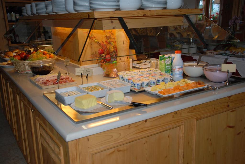 Broša ar dažādiem ēdieniem, tostarp augļiem, gaļu, jogurtu un maizi, izvietota uz koka virsmas.