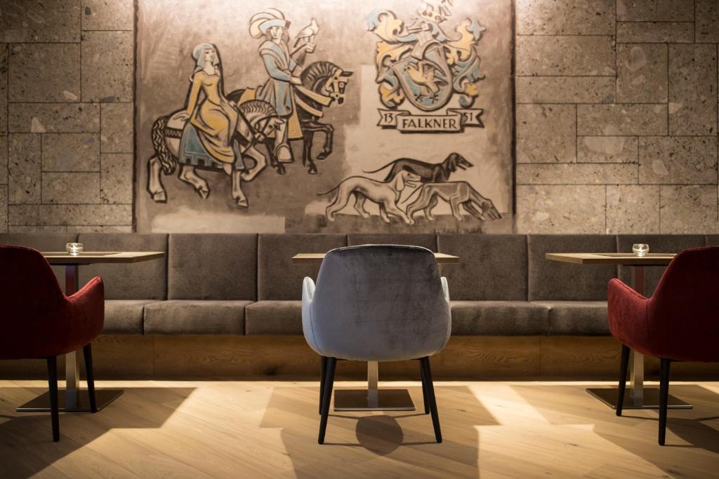 Mūsdienīgs kafijas veikals ar māksliniecisku sienas gleznojumu, kurā attēloti jātnieki un suņi, un stilīgām krēsliem pie galdiem.