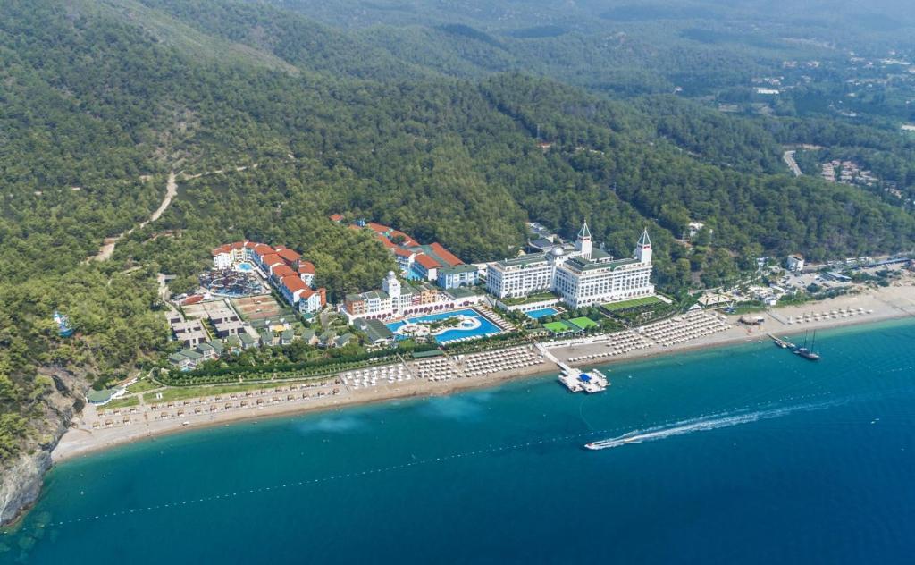 Lidojums virs piejūras kūrorta, kas ietver viesnīcas kompleksu ar baseiniem un pludmales atpūtas zonām, ieskautu zaļojošiem mežiem.