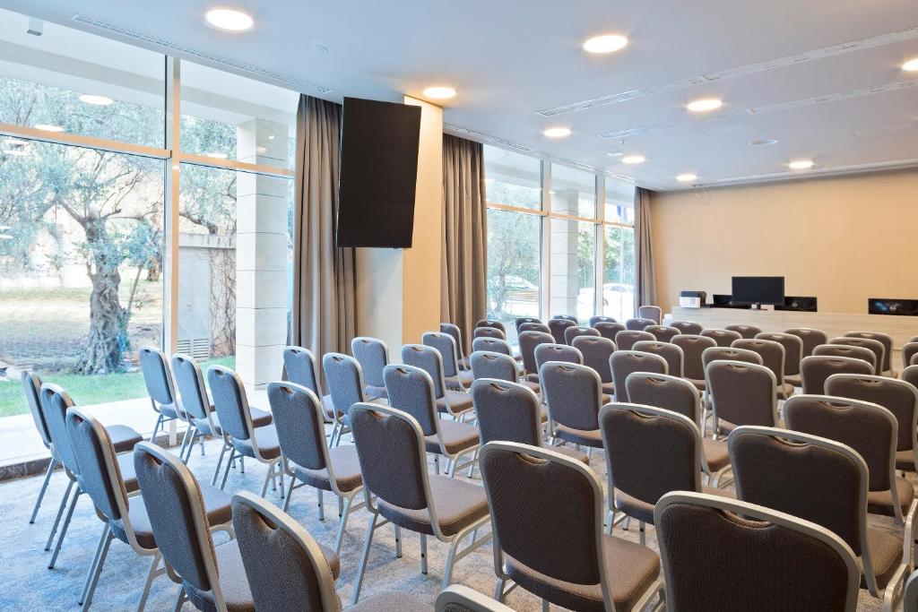 Konferenču zāle ar rindu krēsliem un lieliem logiem, kas nodrošina dabīgu apgaismojumu. Telpa ir aprīkota ar televizoru un prezentācijas iekārtām.
