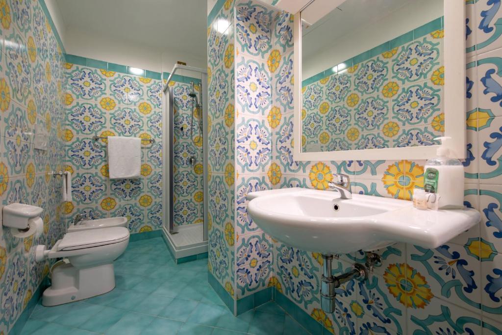 Vannas istaba ar krāsainām flīzēm, dušu un izlietni, kas piepildīta ar higiēnas piederumiem. Mūsdienīgs dizains ar spilgtiem elementiem.