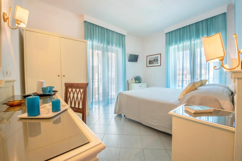 Gaiša un moderna guļamistaba ar lieliem logiem un zilu aizkaru. Uz galda izliktas zilas sveces un dzeramā krūze, radot mājīgu atmosfēru.