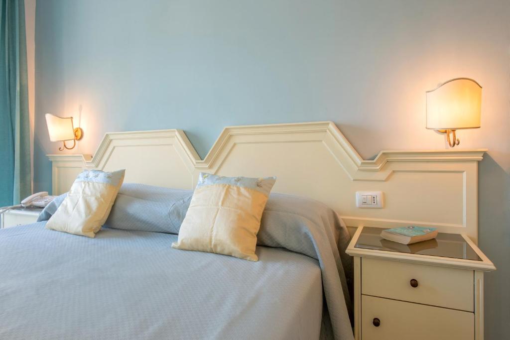 Mūsdienīga guļamistaba ar gaiši zilu sienu, gultu ar spilveniem un elegantu naktsgaldiņu, uz kura atrodas grāmata. Gaismas avoti rada siltu un mājīgu atmosfēru.