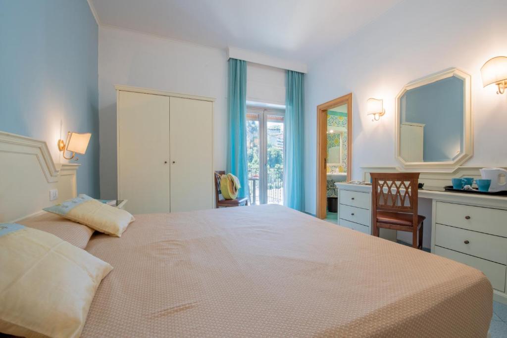 Gaiša guļamistaba ar lielu gultu, elegantu spoguli un koka mēbelēm, kas rada mājīgu atmosfēru. Logi ar gaišām aizkaru drānām piedāvā skatu uz dārzu.