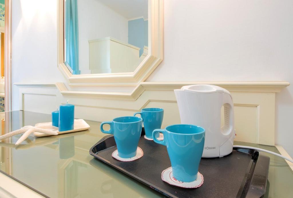 Gaiša istaba ar stikla galdu, uz kura ir trīs zilas krūzes, tējkanna un zila svece. Mirror reflektē telpu un papildina interjeru.