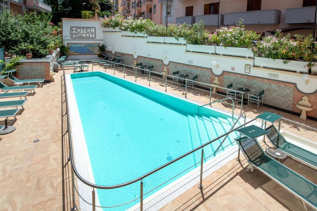 Baseins viesnīcā "Ascot" ar saulainu terasi un atpūtas krēsliem, ideāla vieta relaksācijai un izklaidei. Ziedu kompozīcijas pie baseina piešķir patīkamu atmosfēru.