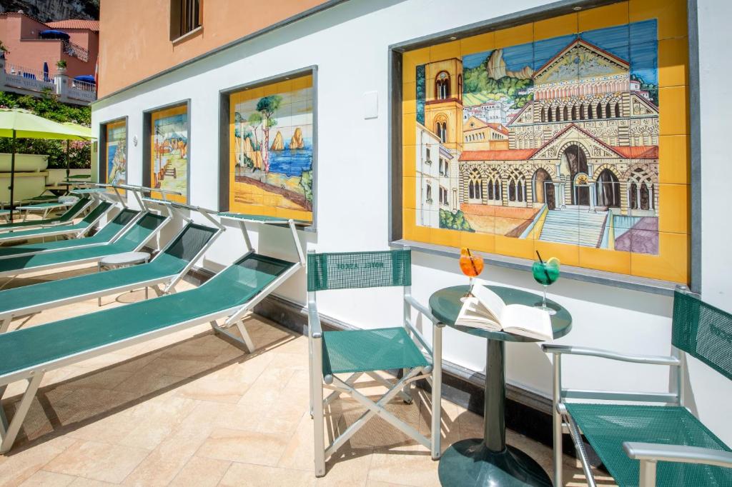 Peldbaseina zona ar saulessargiem, krēsliem un galdu, uz kura atrodas grāmata un dzērieni, fonā ir krāsaini flīžu mākslas darbi.