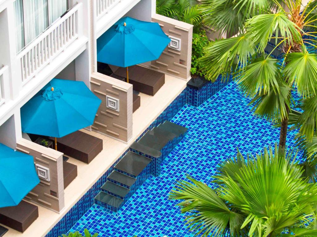 Grand Mercure Phuket Patong baseins ar ziliem saulessargiem un zaļām palmām.