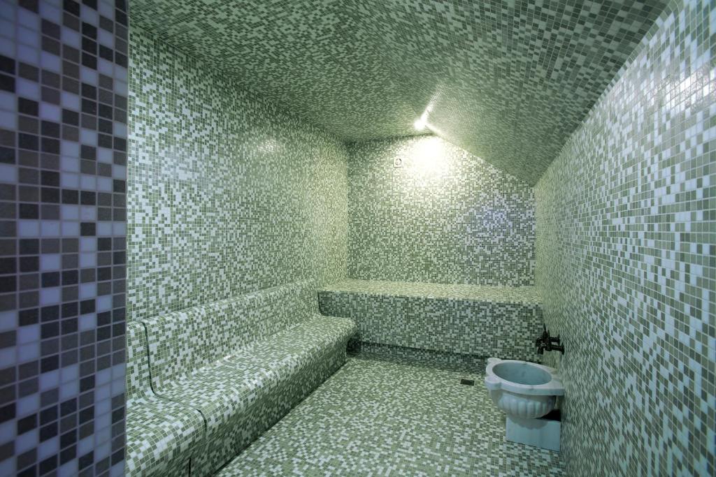 Zaļgana mozaīka tvaika pirts ar sēdvietām un sanitāro ierīci, radot relaksējošu atmosfēru. Ideāla vieta atpūtai un relaksācijai.