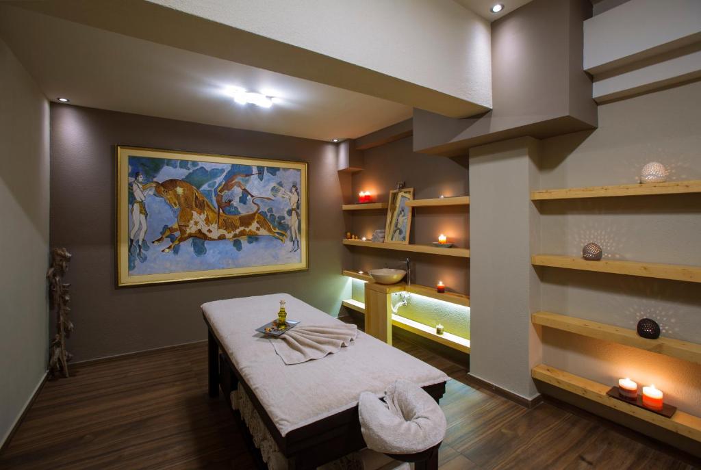 Mūsdienīga spa telpa ar masāžas galdu, dekoratīvām svecēm un mākslas darbu uz sienas, kas rada relaksējošu atmosfēru. Telpas interjers ir siltās krāsās ar koka plauktiem.