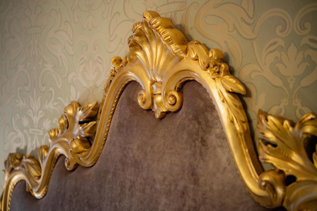 Greznas gultas galvas dēlis ar izsmalcinātu zelta apdari, kas papildina eleganto telpas interjeru. Fons ir zaļā krāsā ar smalku rakstu.