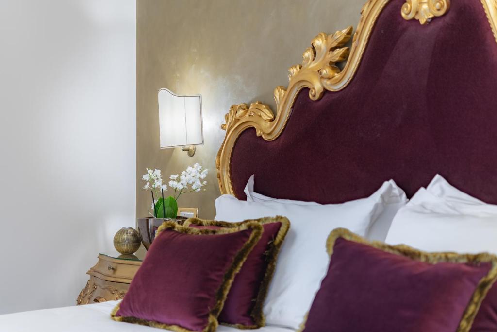 Elegants guļamistabas interjers ar greznu zelta galvgali un purpura spilveniem. Telpā ir arī ziedi un moderns apgaismojums, radot mājīgu atmosfēru.