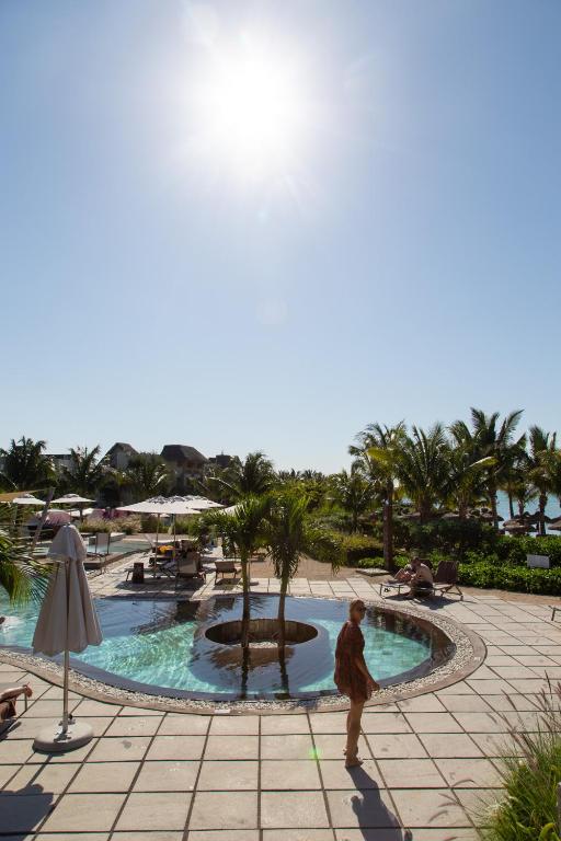 Tropu kūrorta baseins ar palmām, saulains laiks un cilvēki, kas atpūšas malā. Ideāls skats uz atpūtu un relaksāciju pie ūdens.