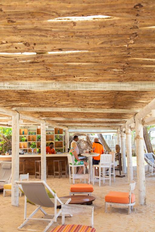 Pludmales bārs ar koka konstrukciju, kur viesi baudījuši dzērienus un atpūtu. Apkārt ir saulaini krēsli un brīva, relaksējoša atmosfēra.