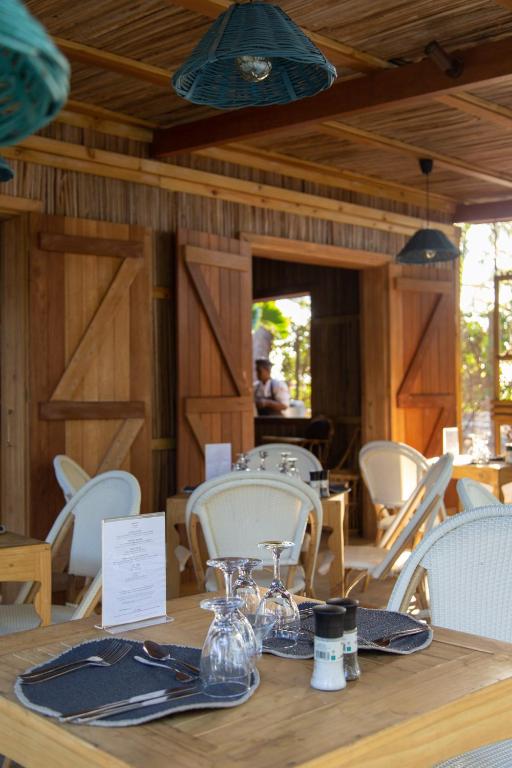 Mūsdienīgs restorāna interjers ar koka un dabīgu materiālu elementiem, kurā redzama eleganta galda uzstādīšana. Gaismas ķermeņi no pīta materiāla un atvērtas durvis rada viesmīlīgu atmosfēru.