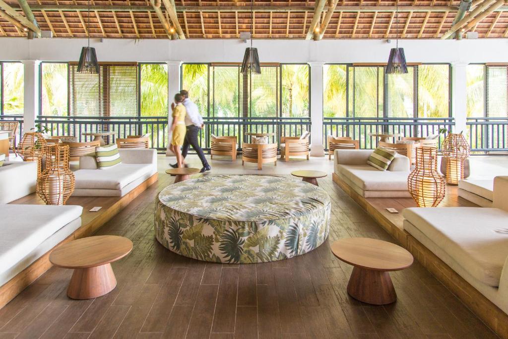 Mūsdienīgs un stilīgs atpūtas telpas interjers ar ērtām mēbelēm un dabīgu apgaismojumu, kurā pāris pastaigājas. Telpā ir zema apaļa galda un sēdvietas ar augu motīviem.