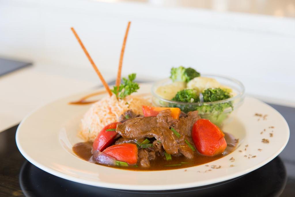 Sastāvdaļu plate ar sautētu gaļu, tomātiem, rīsiem un zaļajiem dārzeņiem, dekorēta ar garšaugiem un kociņiem.