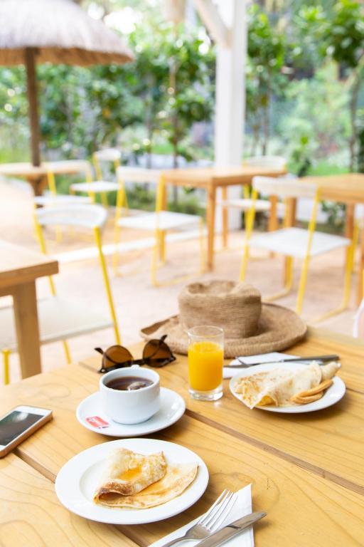 Gardas brokastis ar pankūkām, kafiju un apelsīnu sulu, izvietotas pie elegantā kafejnīcas galda. Daba un moderns interjers rada relaksējošu atmosfēru.