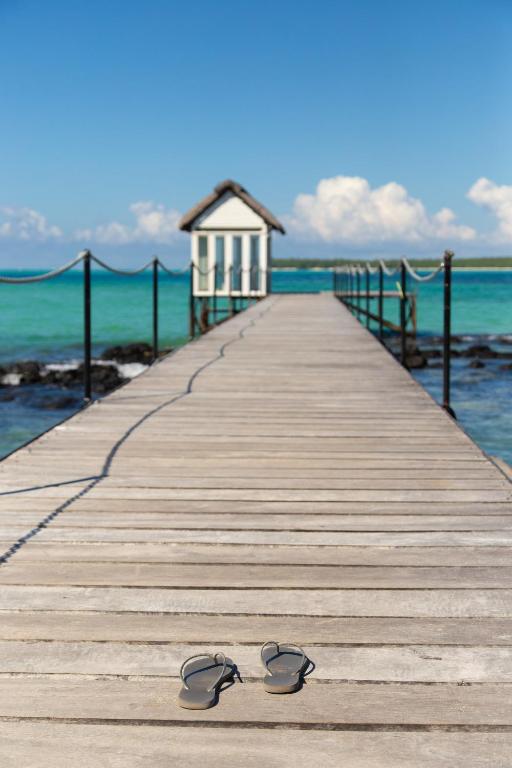 Koka piestātne pie jūras ar skaidru zilu ūdeni un baltām mājiņām. Priekšplānā redzamas čības, kas atstātas uz doka.