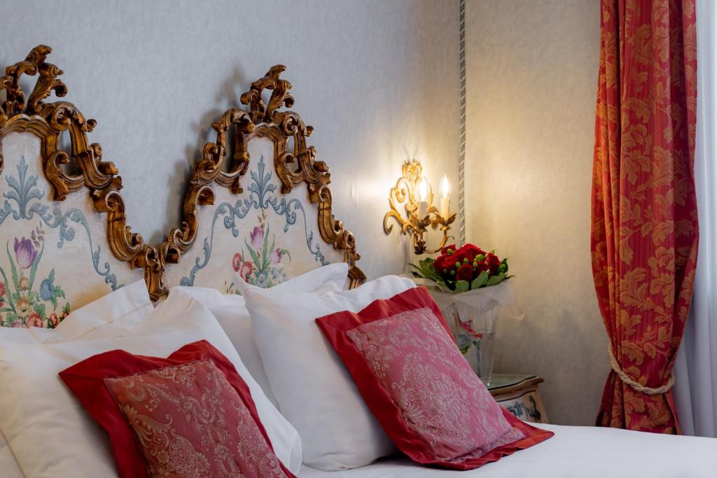 Elegants guļamistabas interjers ar dekoratīviem gultas galviņām, mīkstām spilveniem un siltu apgaismojumu. Sarkanās aizkaru un ziedu kompozīcijas piešķir telpai viesmīlīgu atmosfēru.