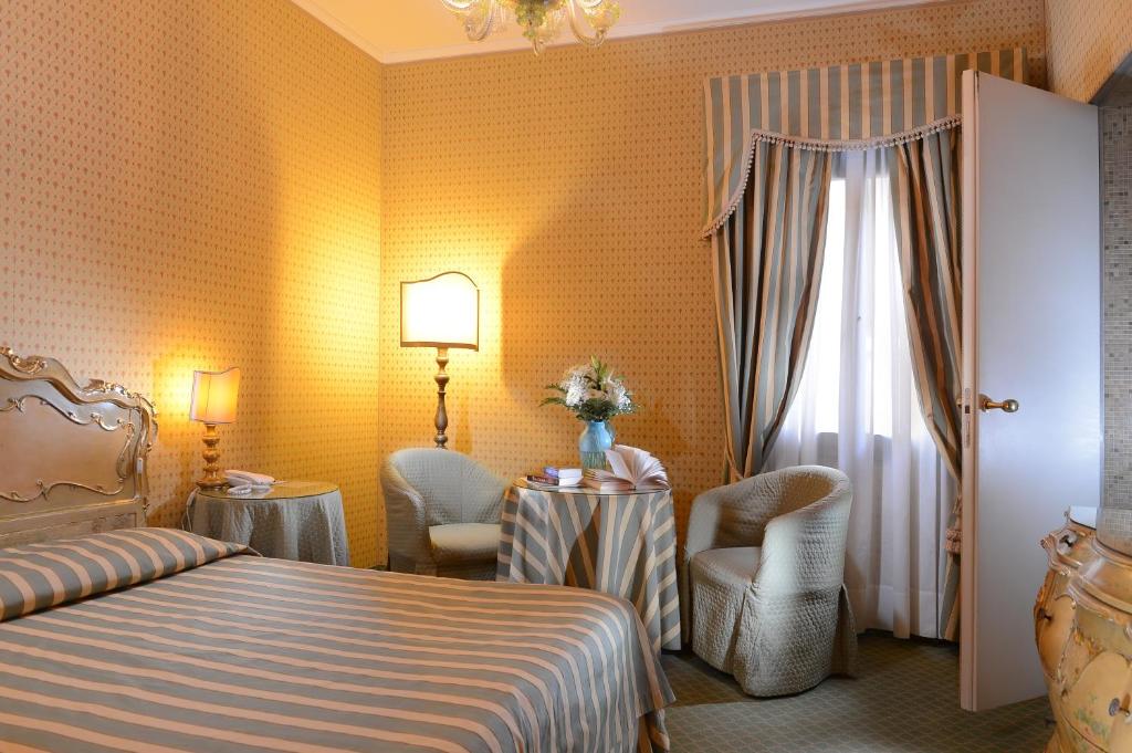 Elegants viesnīcas numurs ar gaišām sienām un harmonisku interjeru, kurā ir gultas ar svītrām, mīkstas krēsli un galds ar ziediem. Ideāla atmosfēra relaksācijai un komfortam.